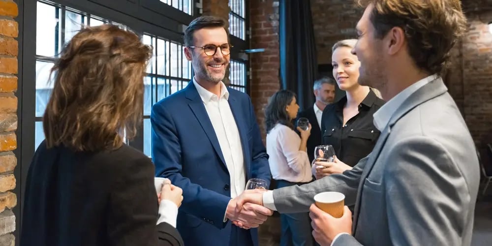 Professionals coordinating and shaking hands at a conference event, representing collaboration between teams in complex event environments.