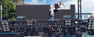 Event crew assembling stage lighting and equipment, highlighting behind-the-scenes event setup and communication coordination during build-out.
