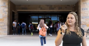 School administrator using a handheld radio as students arrive on campus, demonstrating how effective communications help create safer schools.