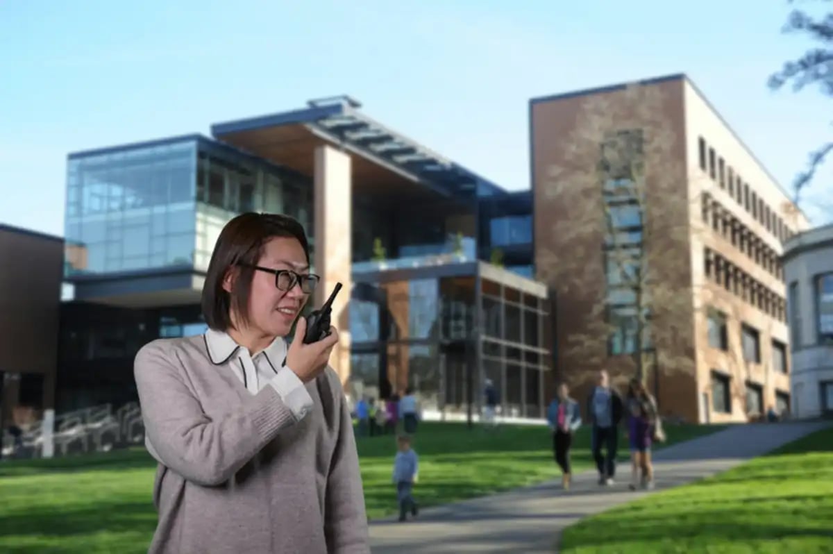 School staff member using a two-way radio outside a campus building to support day-to-day school communications and emergency response coordination.