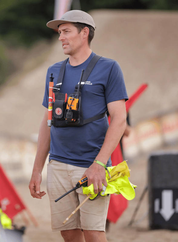 Event crew member with a two-way radio speaks with people beside the race course.